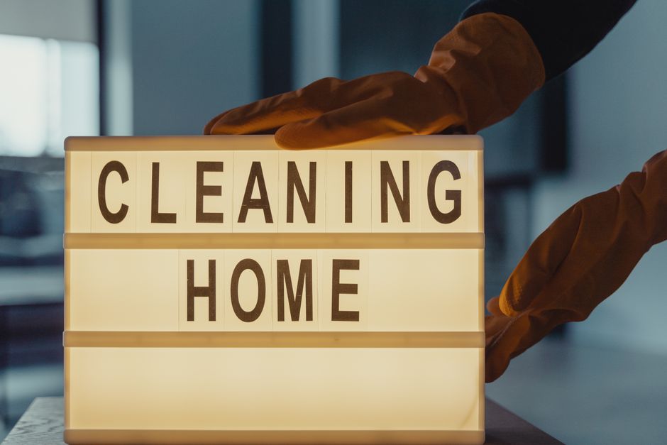 Latex-gloved hands holding a lightbox sign with 'CLEANING HOME' text.